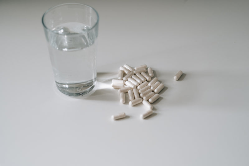 bicchiere d'acqua e pillole su un bancone bianco