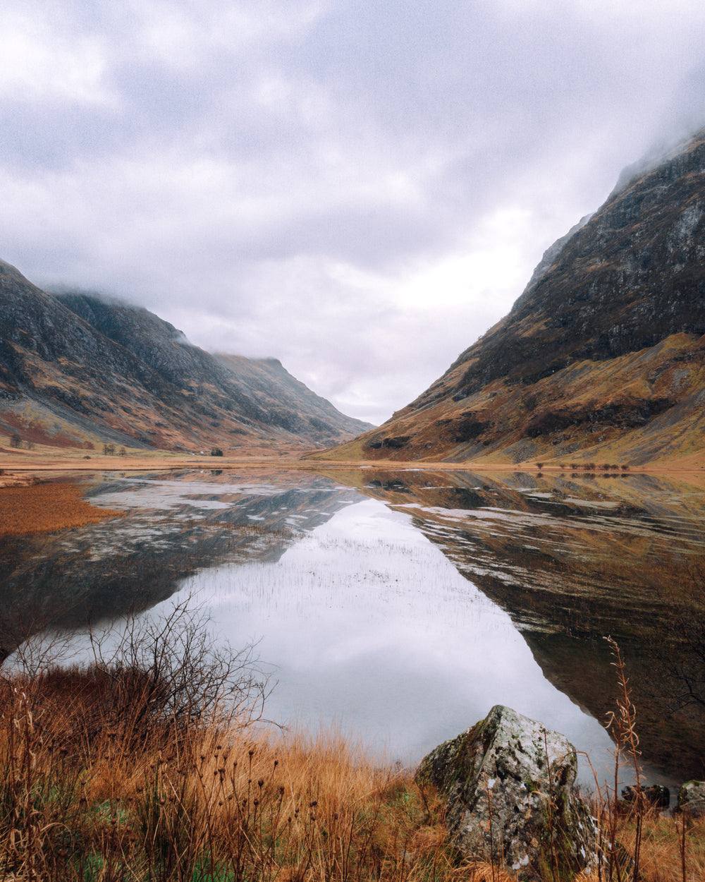 glassy lake reflecting cloud covered mountains