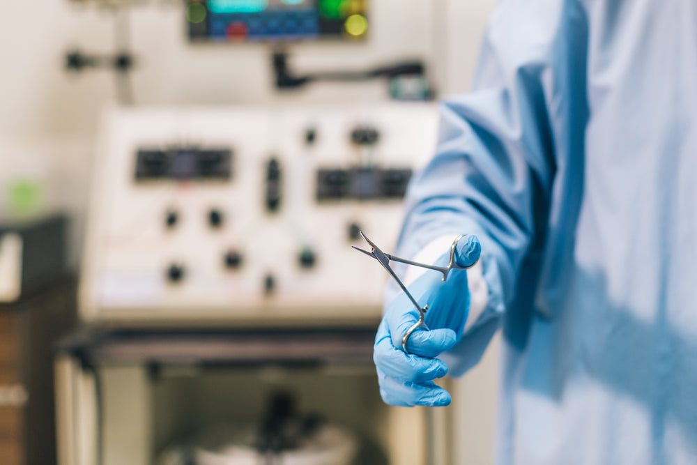 gloved hand of doctor in scrubs holds straight forceps