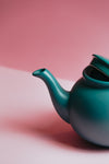 green teapot against a light pink backdrop