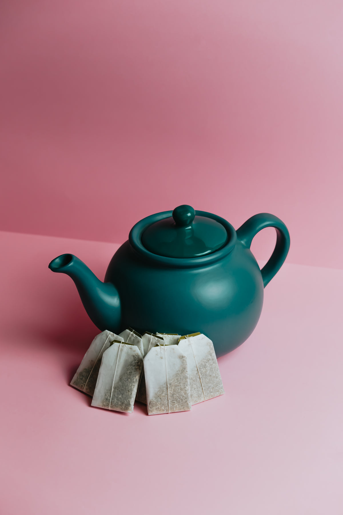 green teapot sits on a pink background with fresh tea bags