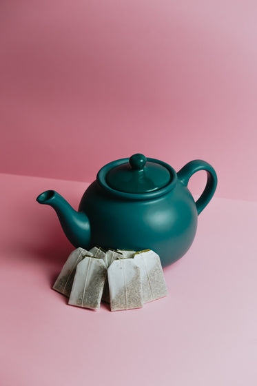 green teapot sits on a pink background with fresh tea bags