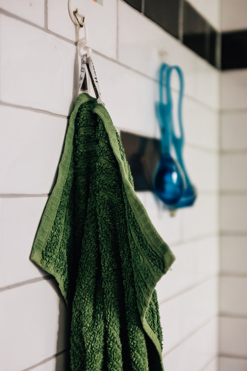 green towel hands on white tiled wall