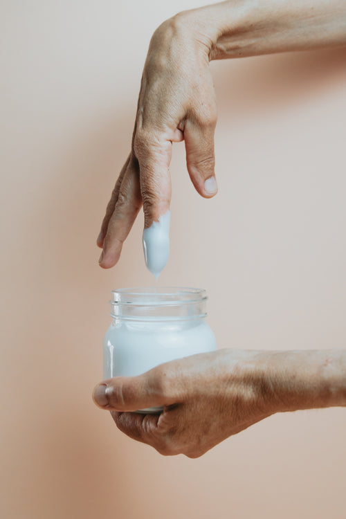 hand and a glass jar of hand cream