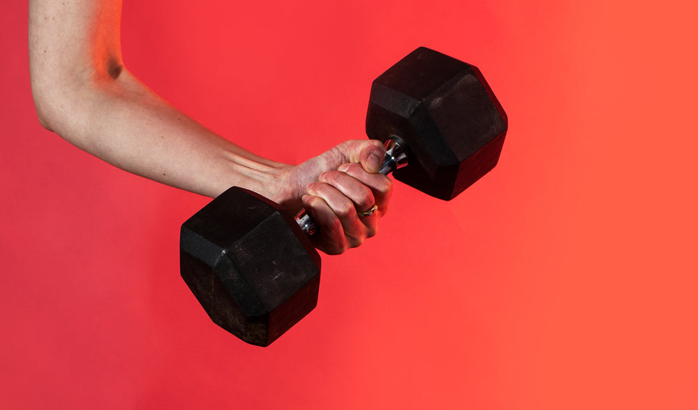 hand grips a dumbbell against a vibrant red background