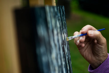 hand holding a fine paint brush to a painting