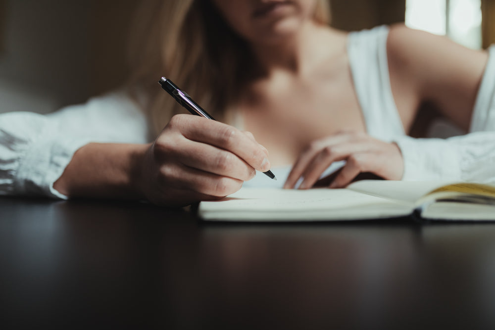 hand holding a pen over a notebook over black table