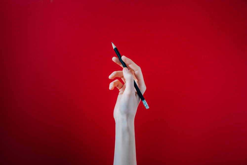 hand holding black pencil on red background