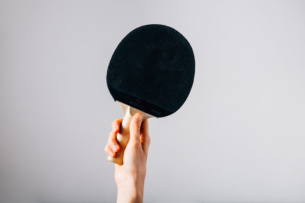 hand holding ping pong paddle on grey background