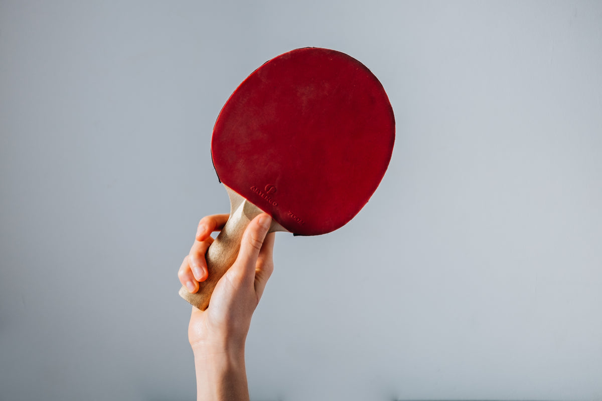 Hand Holding Red Ping Pong Paddle On Grey Background