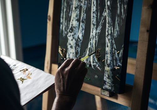 hand holds a brush to canvas painting of birch trees