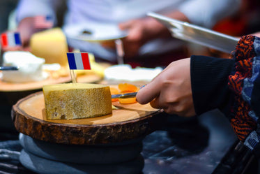 hand holds a cheese knife to a block of cheese