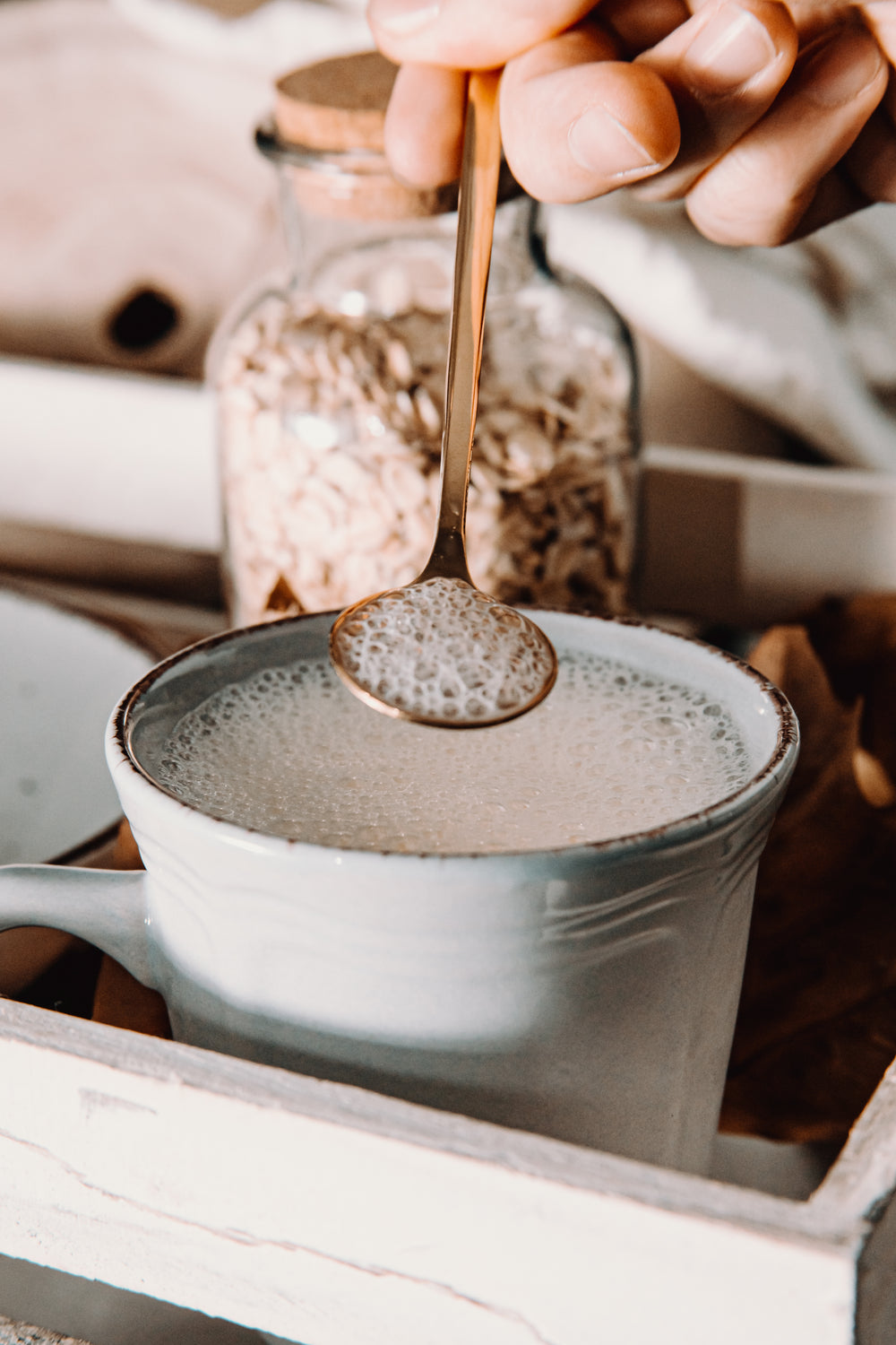 hand holds a gold spoon over a mug filled with foamy milk