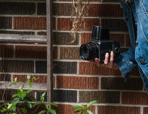 hand holds a hasselblad camera standing by a brick wall