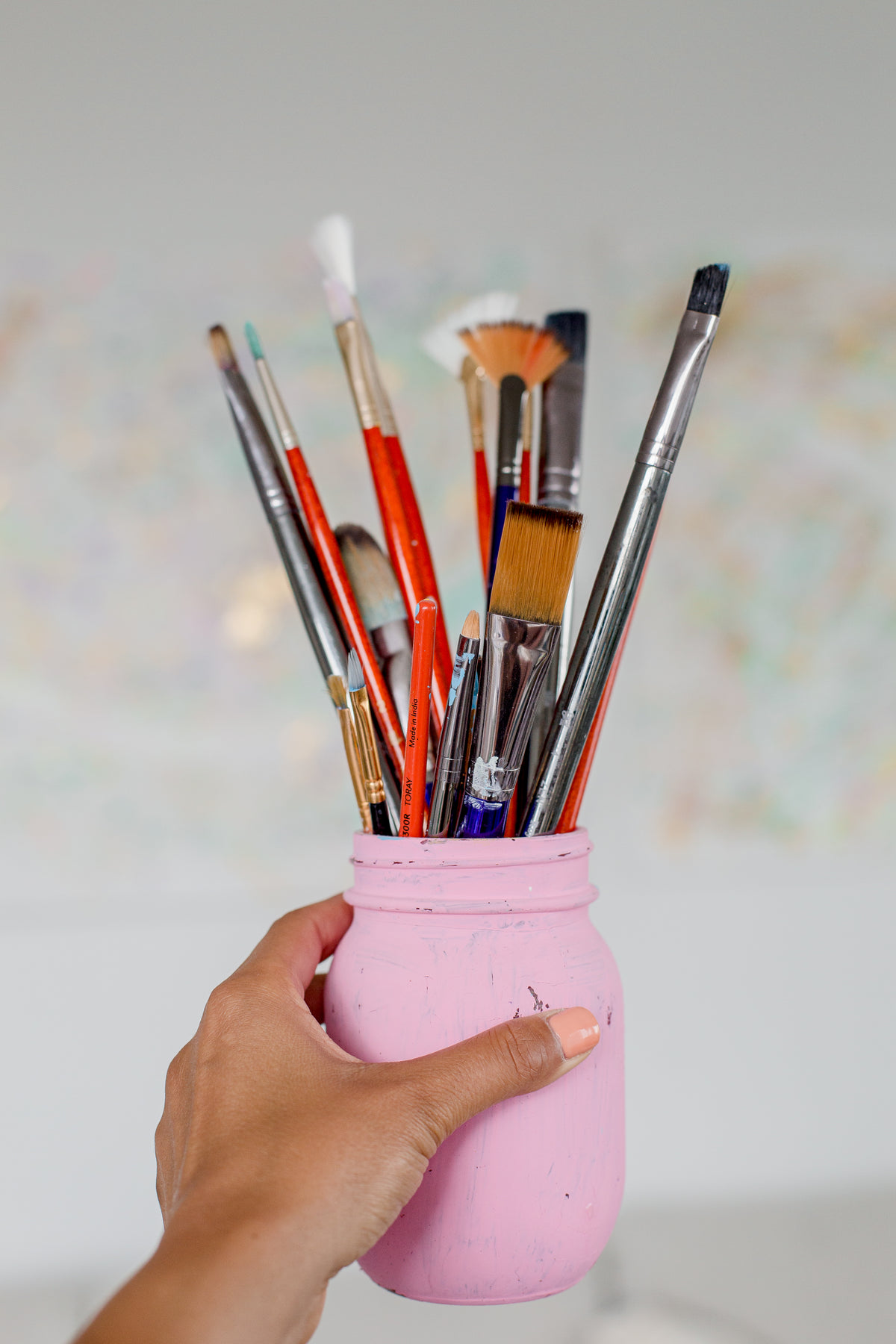 hand holds a pink mason jar filled with paint brushes