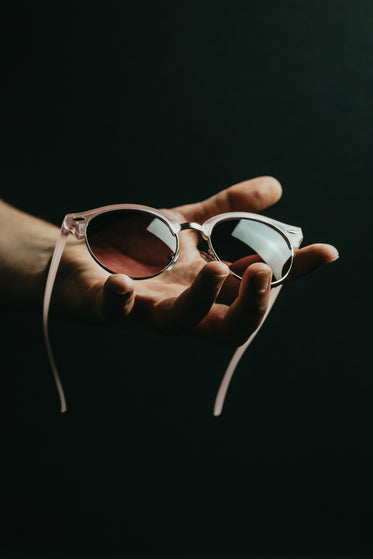 hand holds a pink sunglasses with a open palm