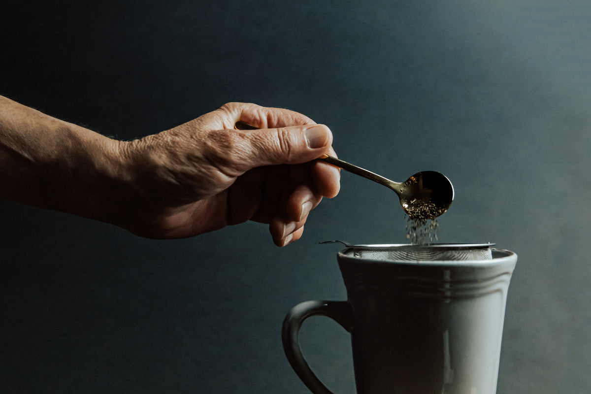 hand holds a spoon and adds loose leaf tea to a mug