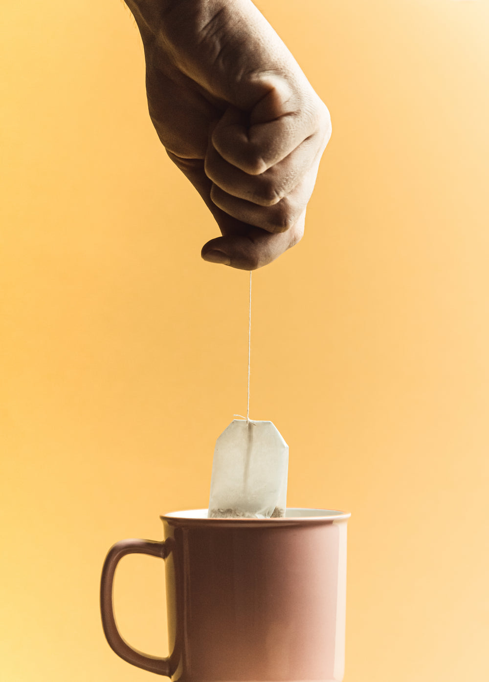 hand holds a tea bag over a cup