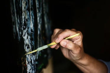 hand holds a yellow paint brush to a painting of trees