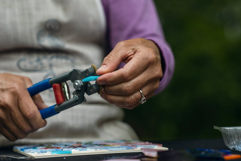 hand holds blue glass to cutting tool to cut it