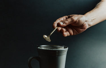 hand holds loose leaf tea over a mug with a stainer