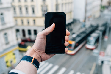 hand holds out a black cell phone with scenery out of focus