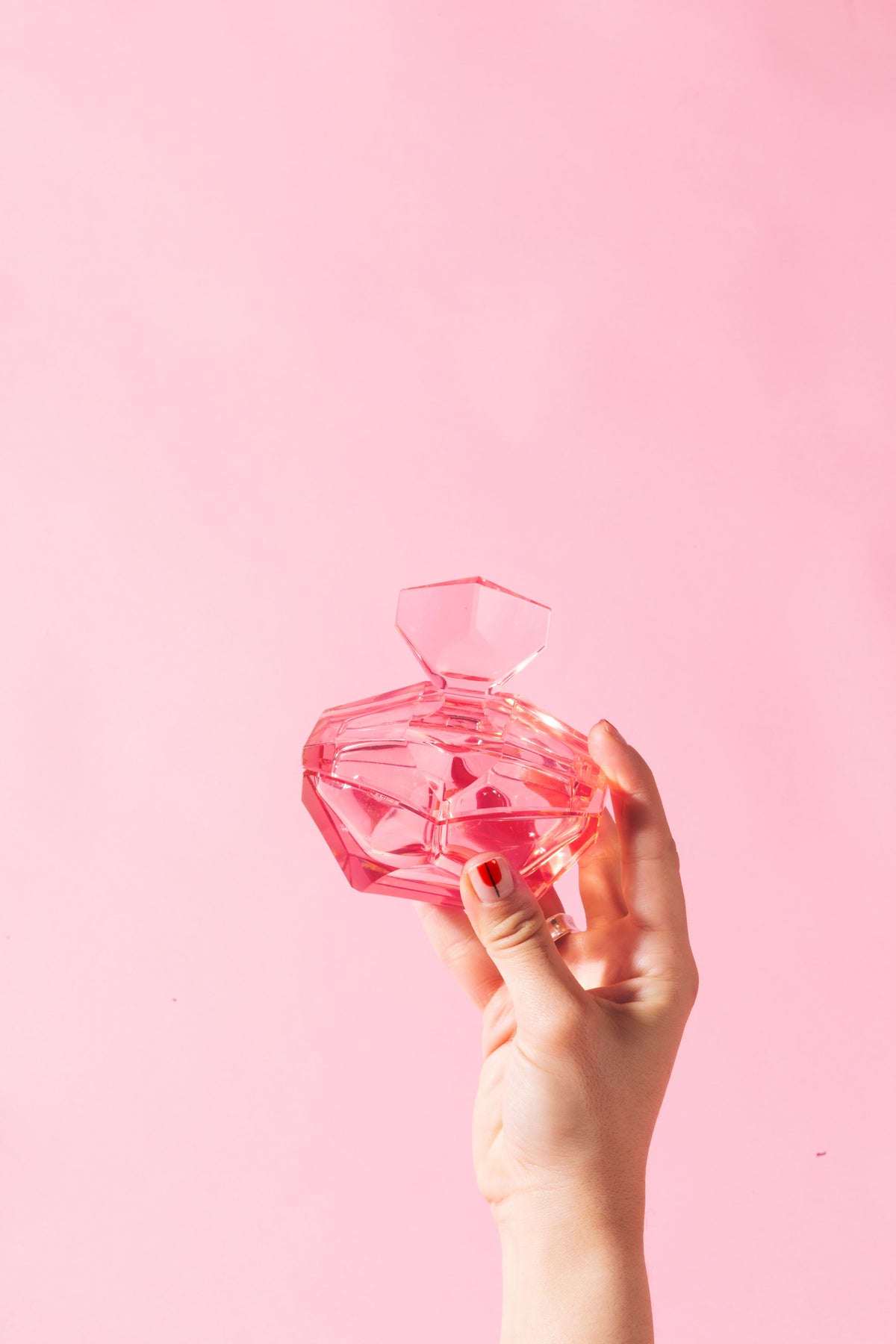 hand holds pink glass bottle against pink