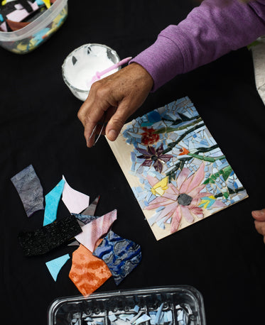 hand holds tweezers above glass mosaic of flowers