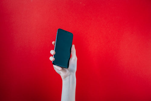 hand holds up black mobile phone on red background