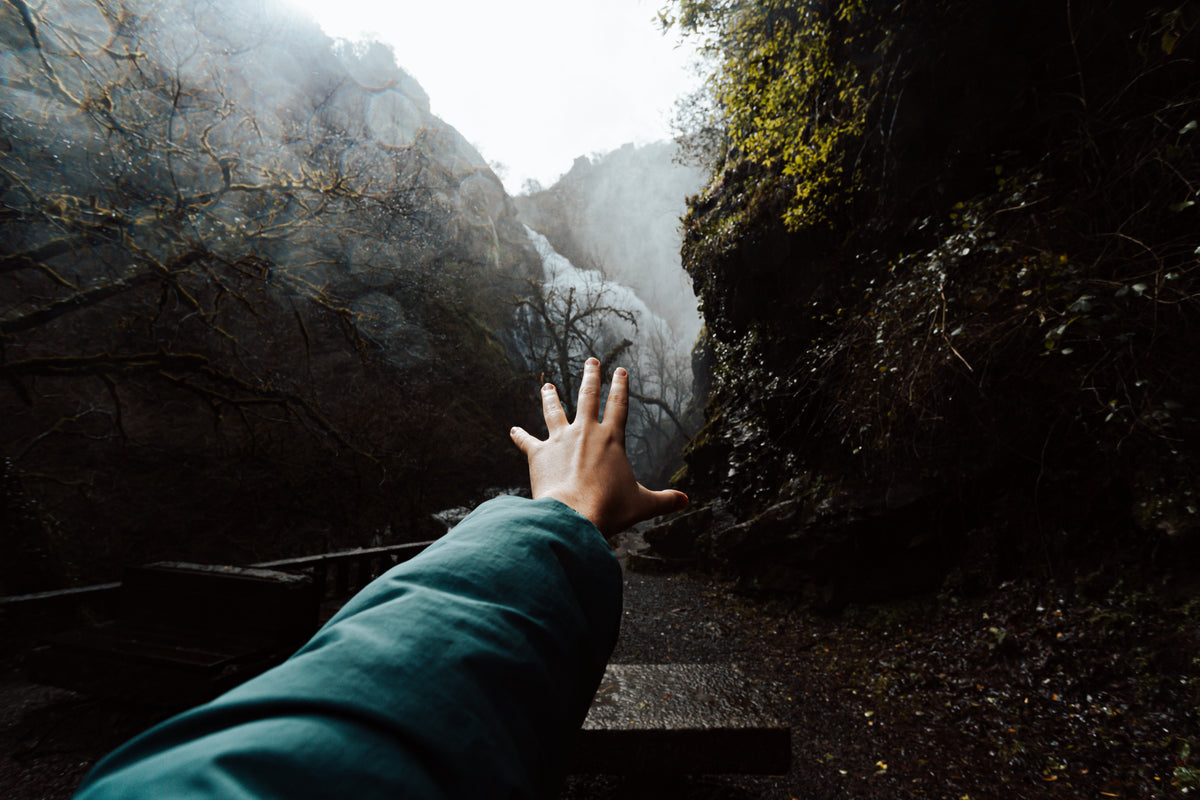 hand reaches toward a waterfall from between two hills