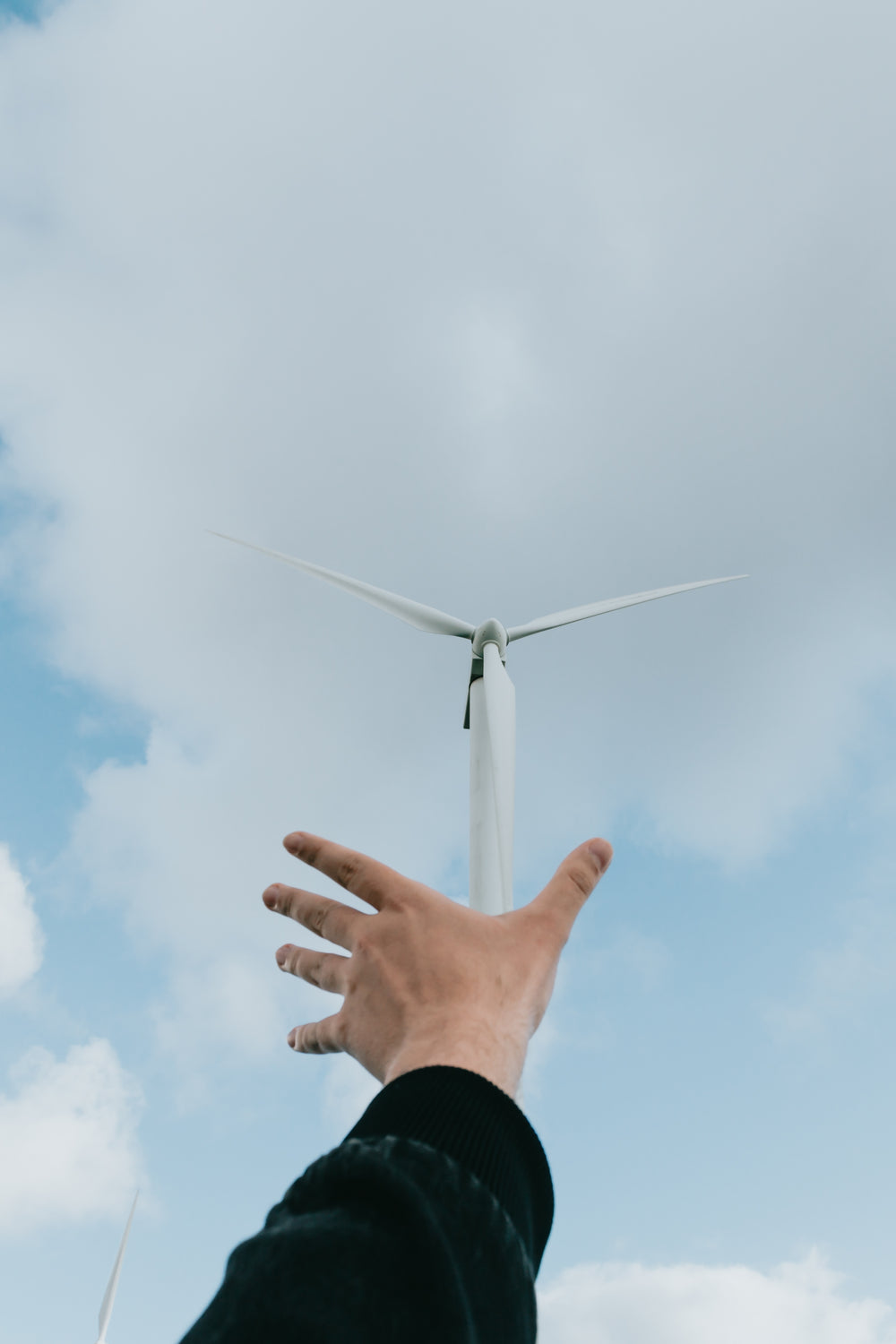 hand reaches towards a windmill on a clear day