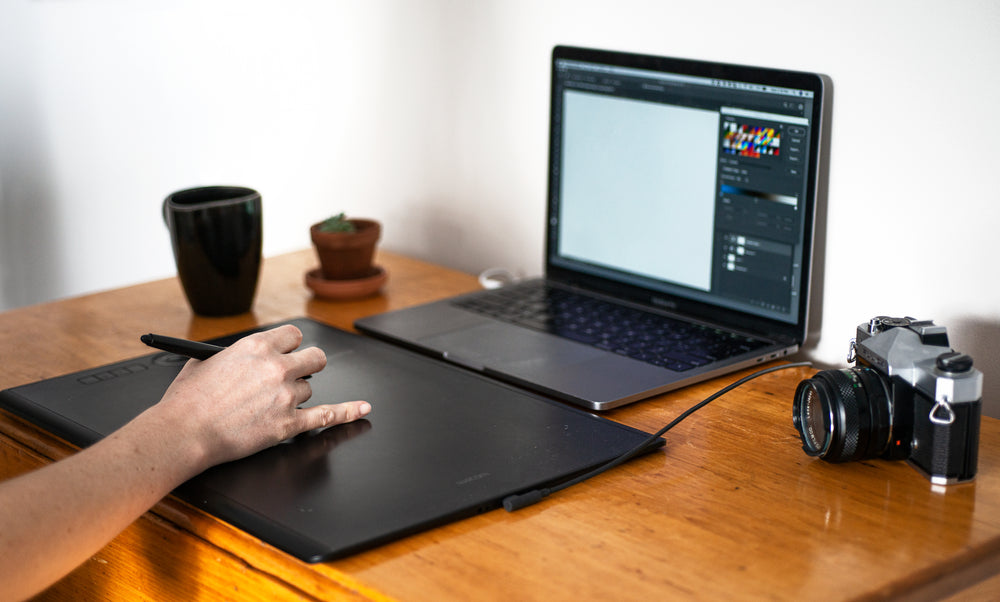 hand uses a pen on a large tablet in front of a laptop