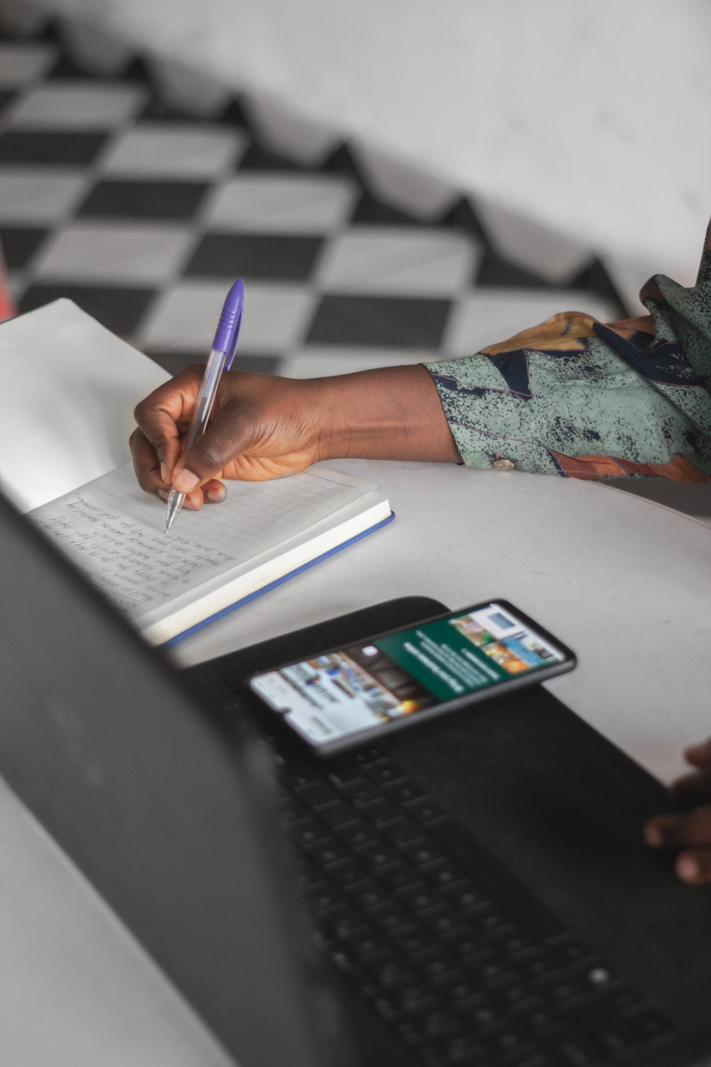 hand writes in a notebook by a laptop and cellphone