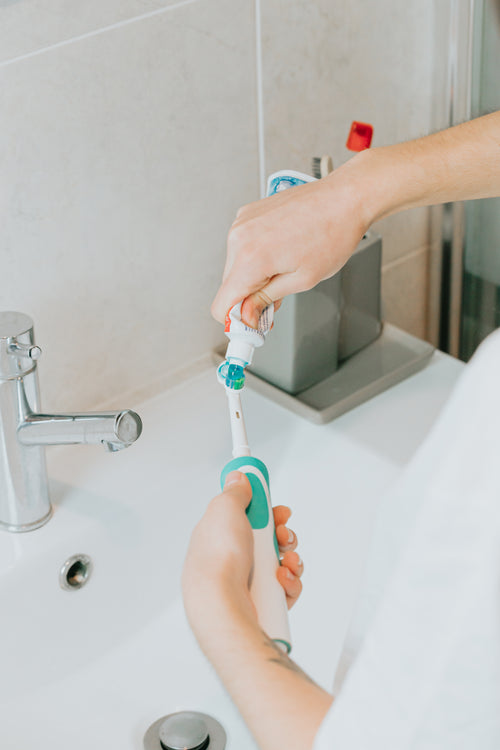 hands adding toothpaste to an electric toothbrush