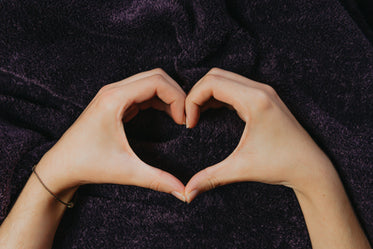 hands create a heart shape against a blanket
