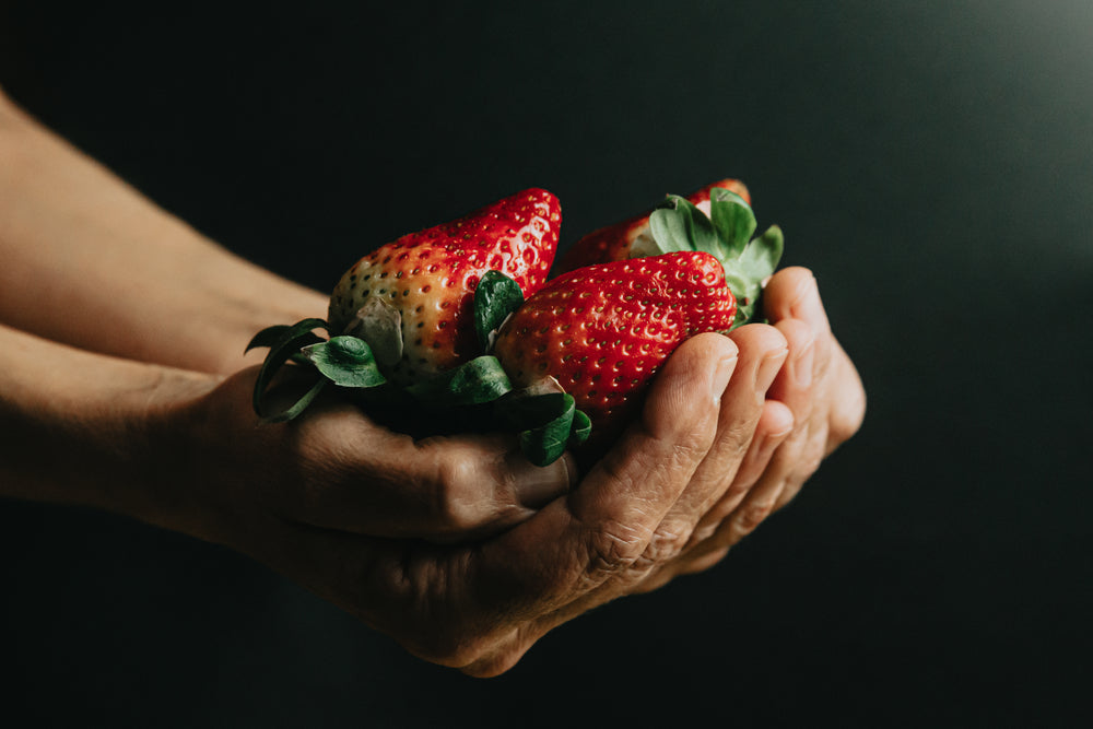 hands filled with ripe strawberries on black background