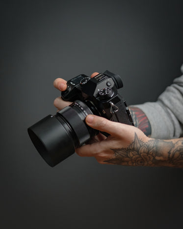 hands hold a black camera against a grey background