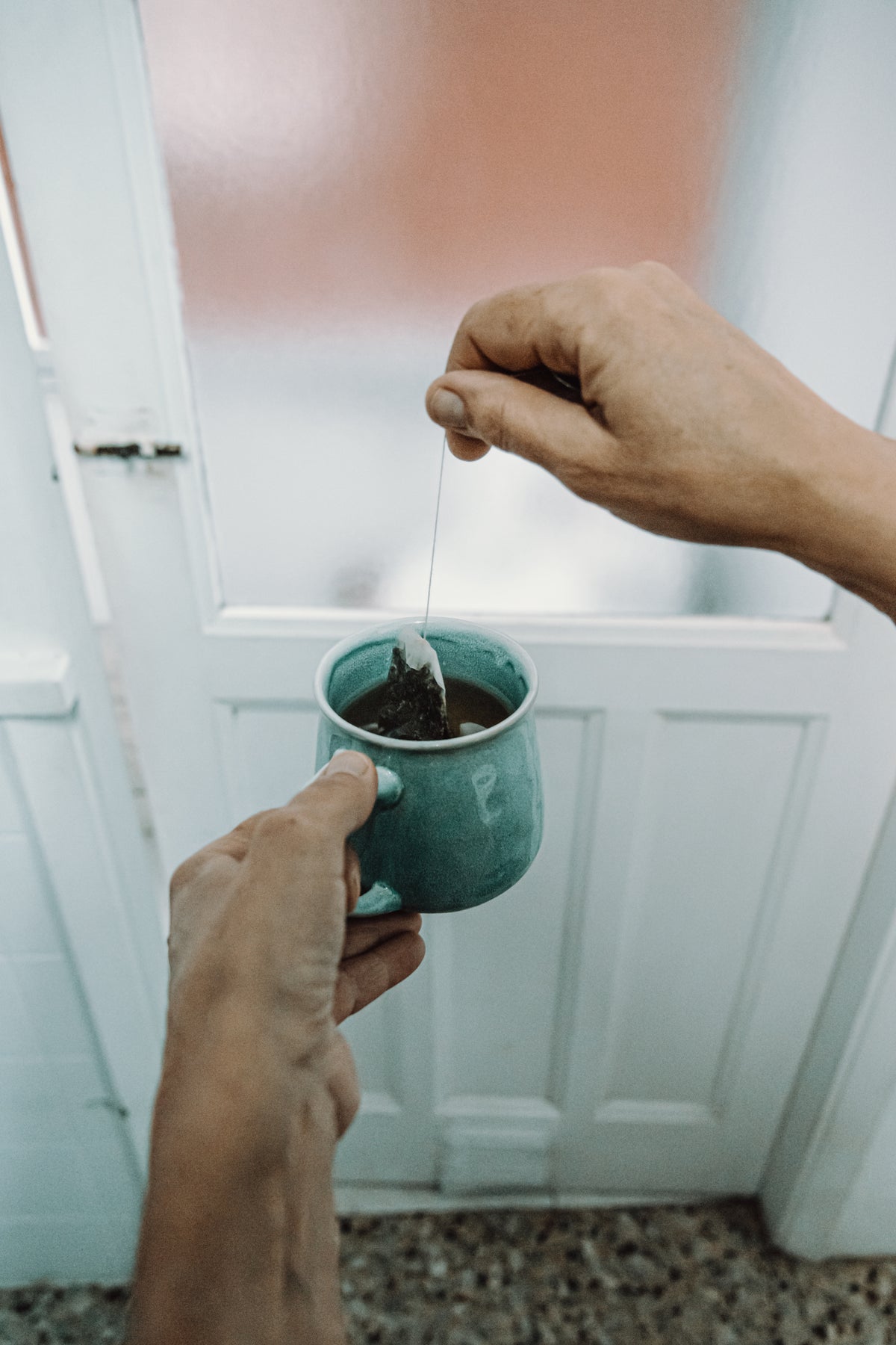 hands hold a tea bag and mug in front of a door