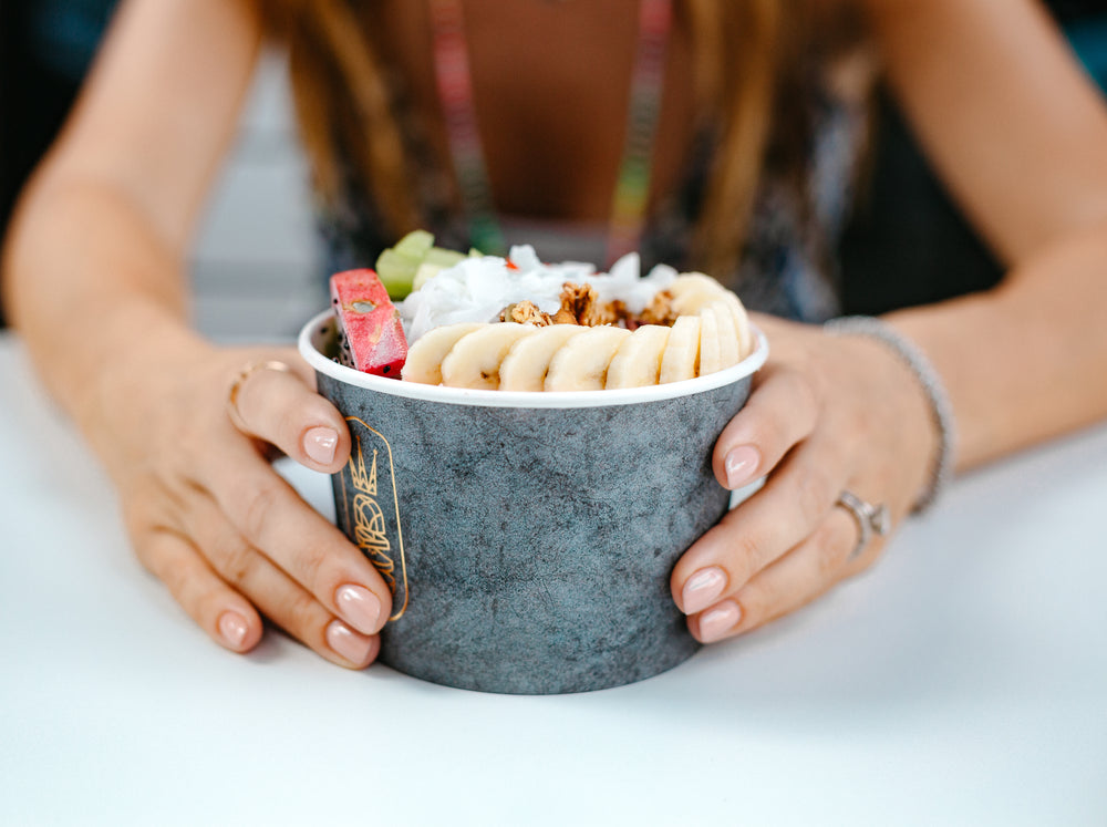 hands hold bowl full of fruit and granola