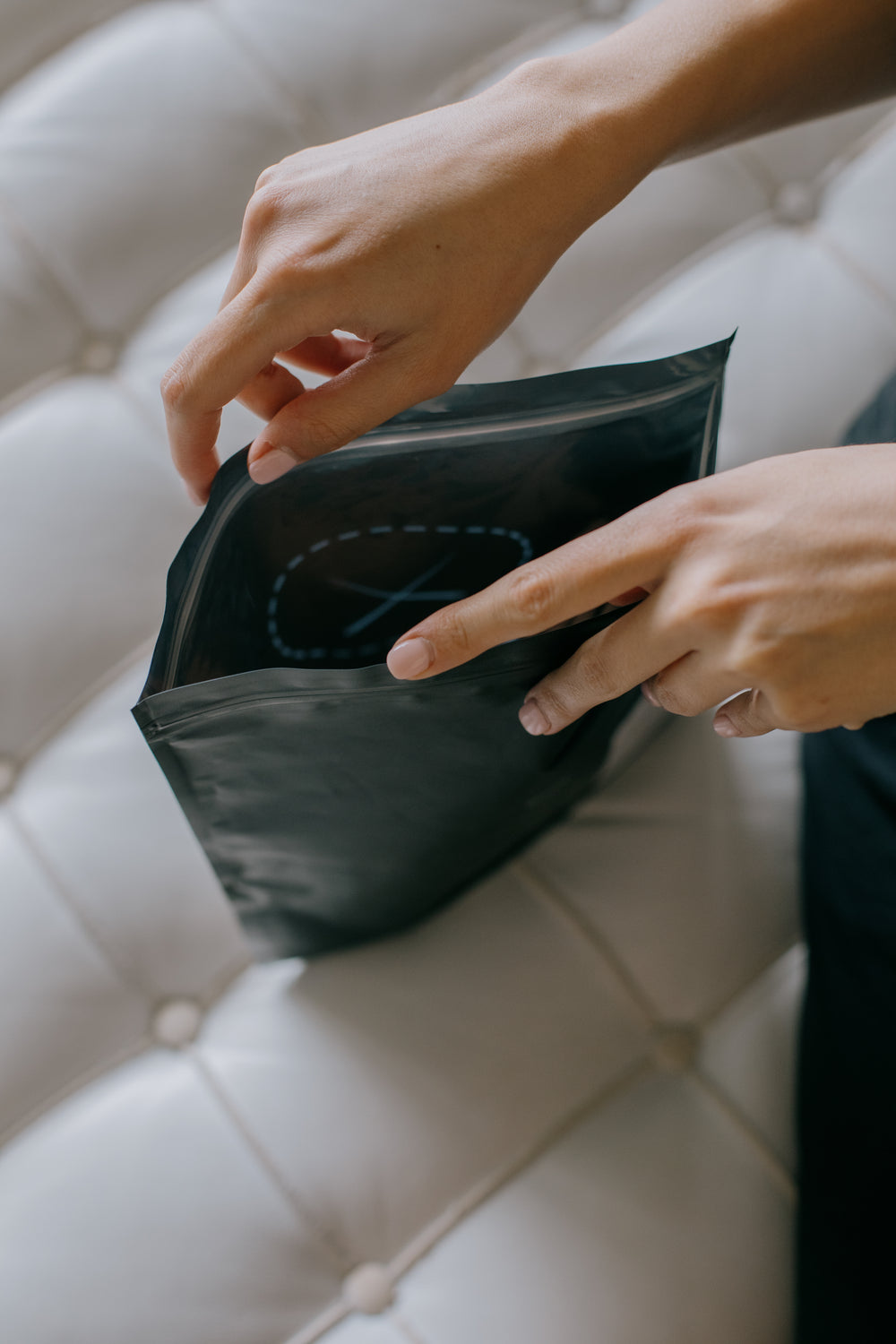 hands hold open a black plastic envelope on couch