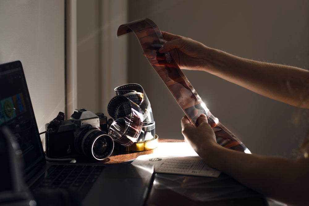 hands hold out film negatives to view them over a wooden desk