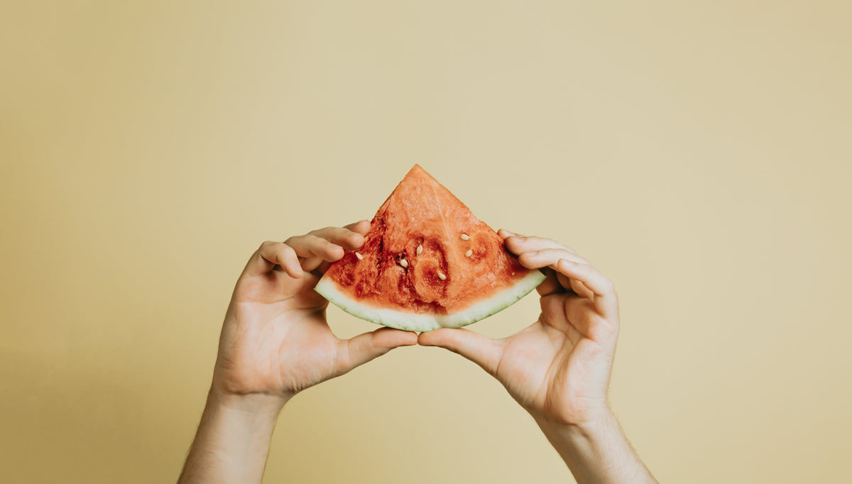 hands hold up a slice of watermelon against yellow