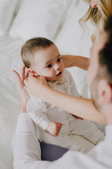 hands holding a baby in a dress shirt and bowtie