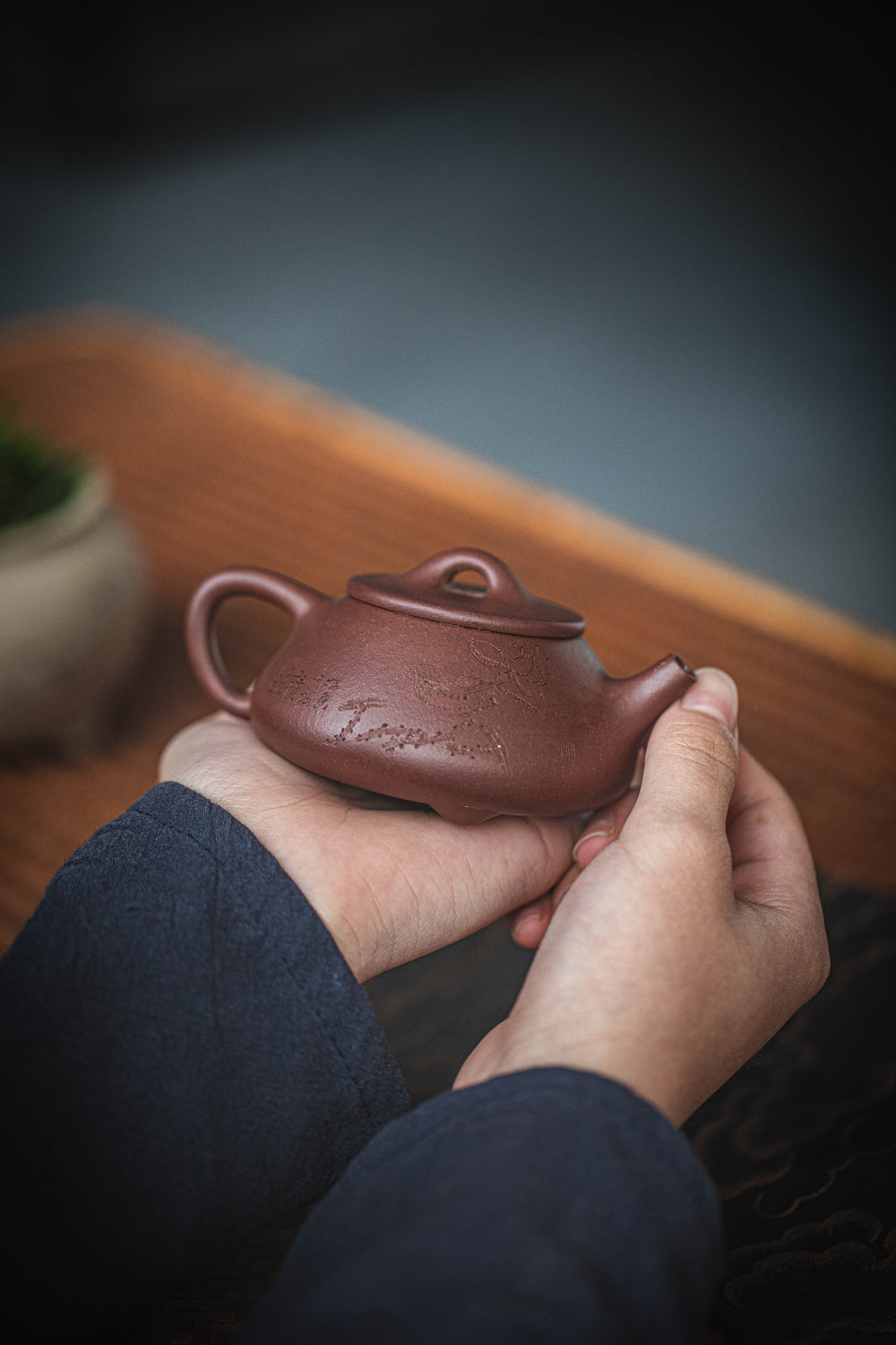 hands holding a carved chinese teapot