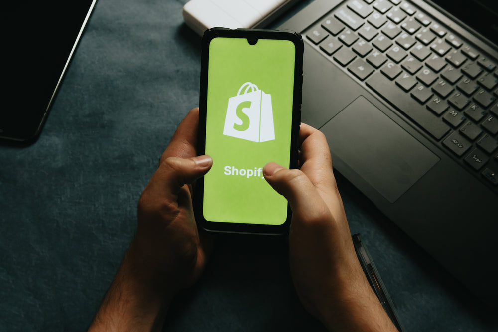 hands holds a cell phone showing the shopify logo