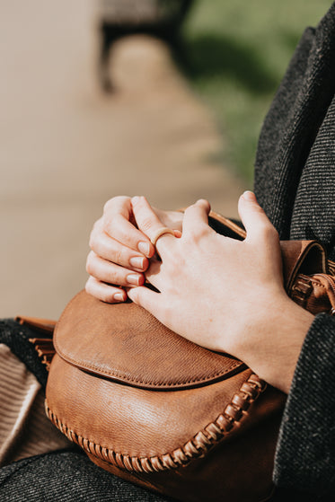 hands lay on a brown leather bag on a persons lap