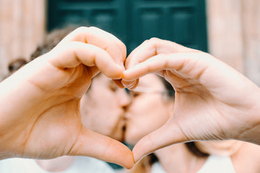 hands meet to form a heart and frame kissing couple