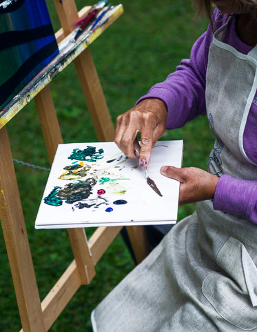 hands mix paint on a white pallet with a pallet knife