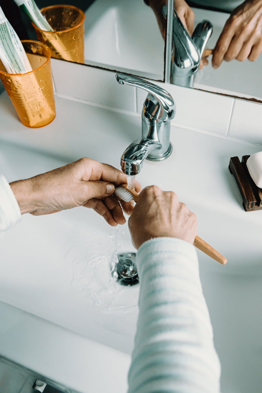 hands rinse out a wooden toothbrush in a white sink