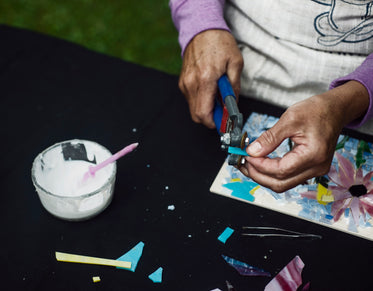 hands trim blue glass for a mosaic of flowers